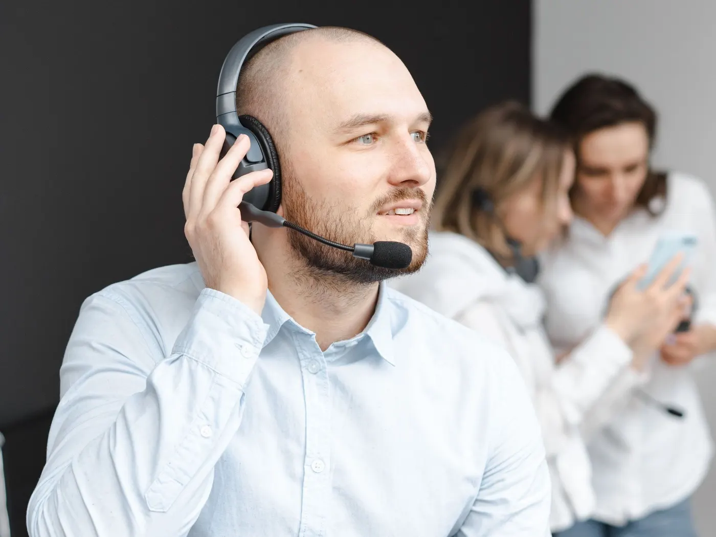 Mosolygó értékesítő headsettel telefonál, mögötte két kollégája